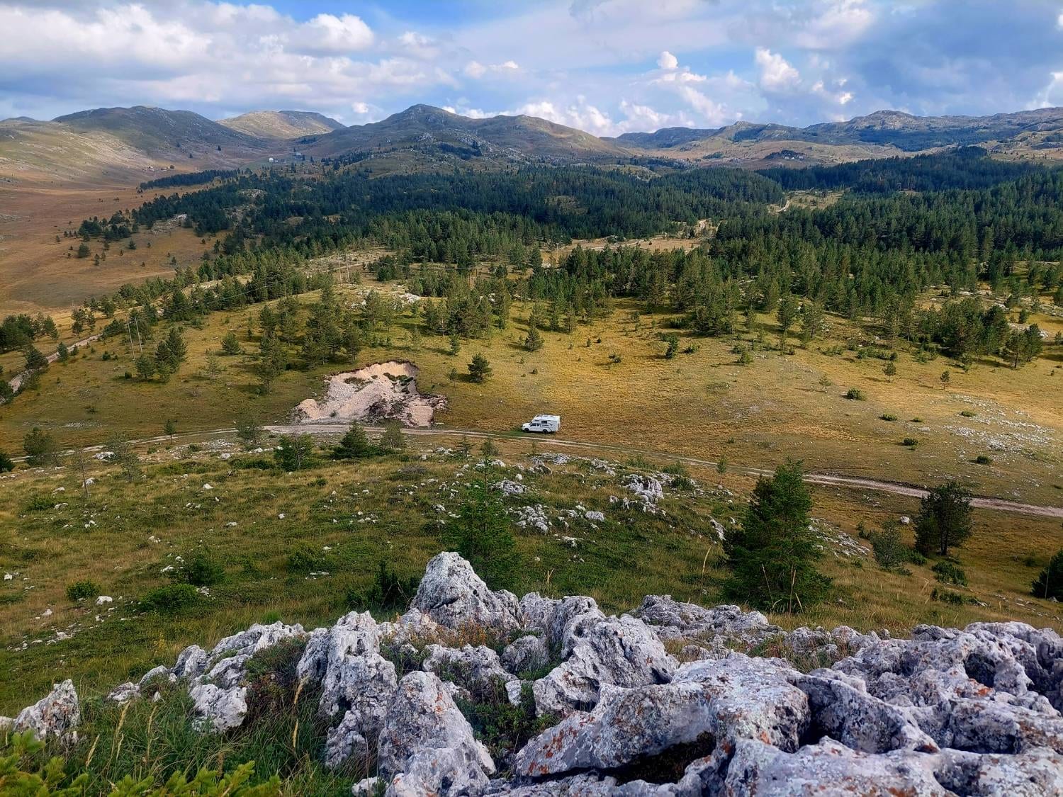 Rancherita en una pista entre pastos y pinos, con las montañas de los Balcanes al fondo