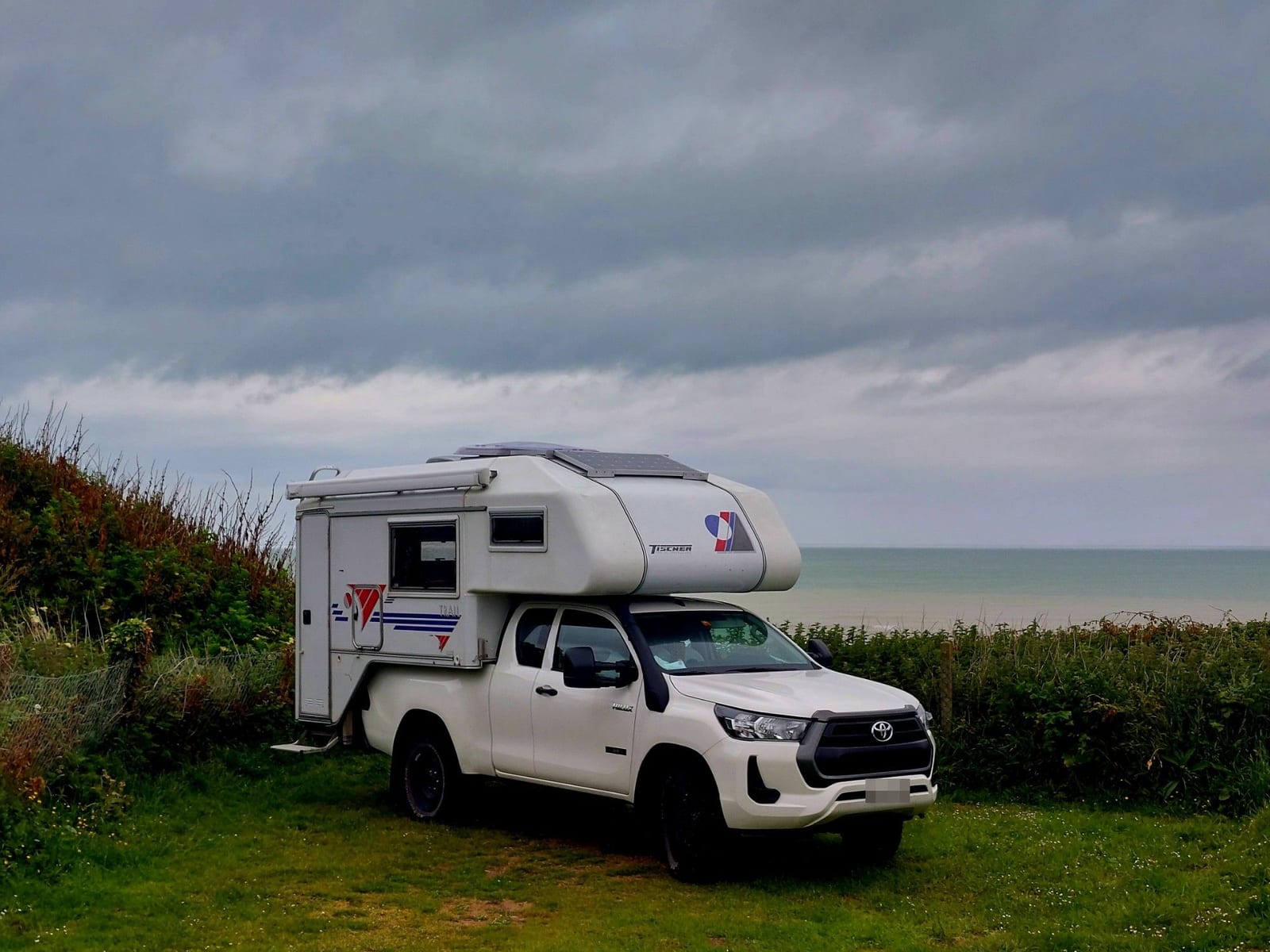 Rancherita aparcada sobre la hierba junto al mar, bajo un cielo gris